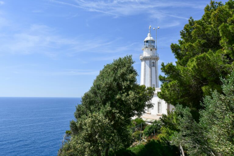 Scenic view of a lighthouse by the Mediterranean Sea in Jávea, Spain with lush greenery.