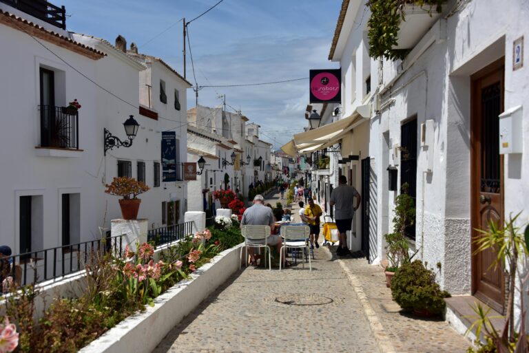 Enchanting cobblestone alley in Altea, Spain, with sunlit white buildings and a lively atmosphere.