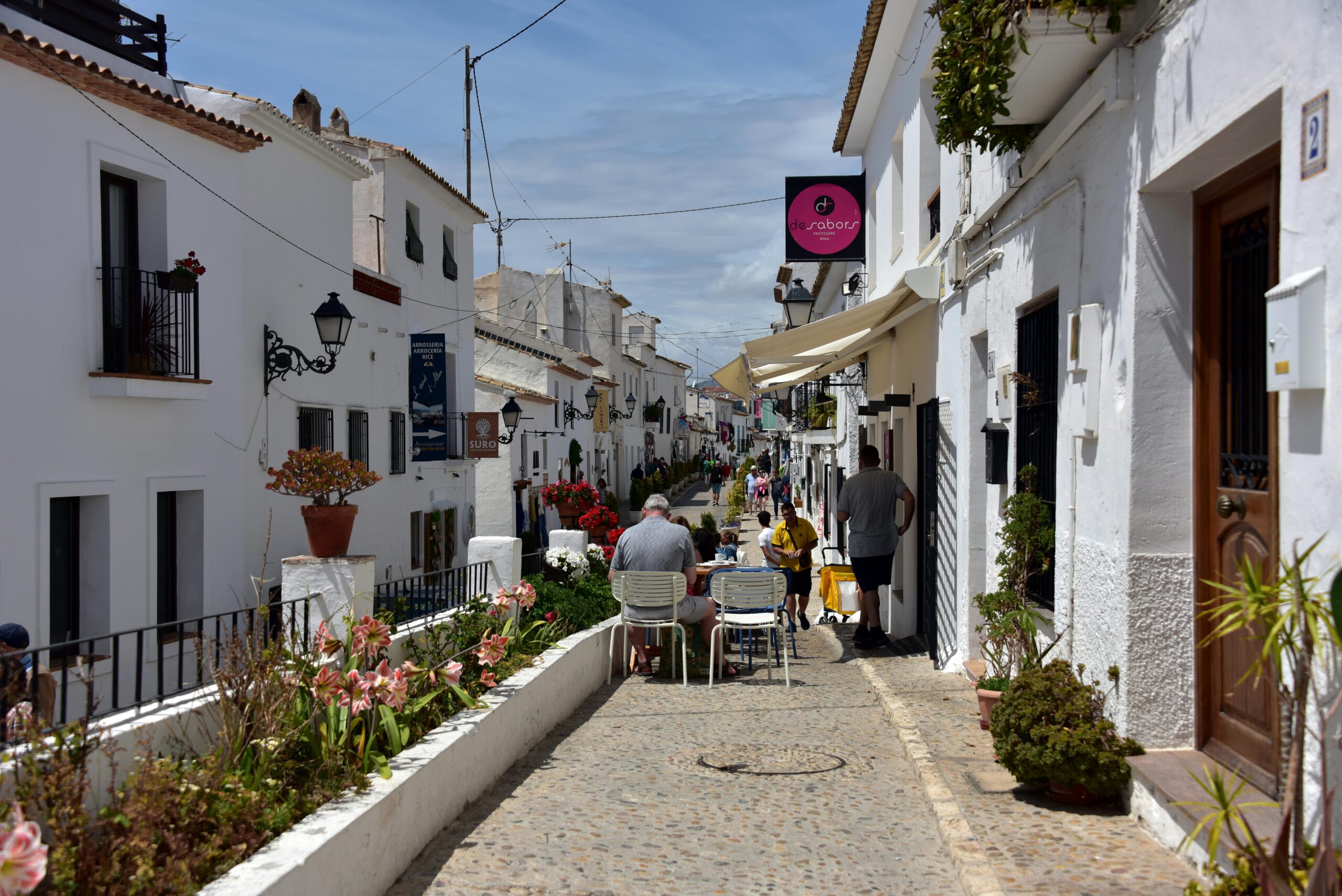 Enchanting cobblestone alley in Altea, Spain, with sunlit white buildings and a lively atmosphere.