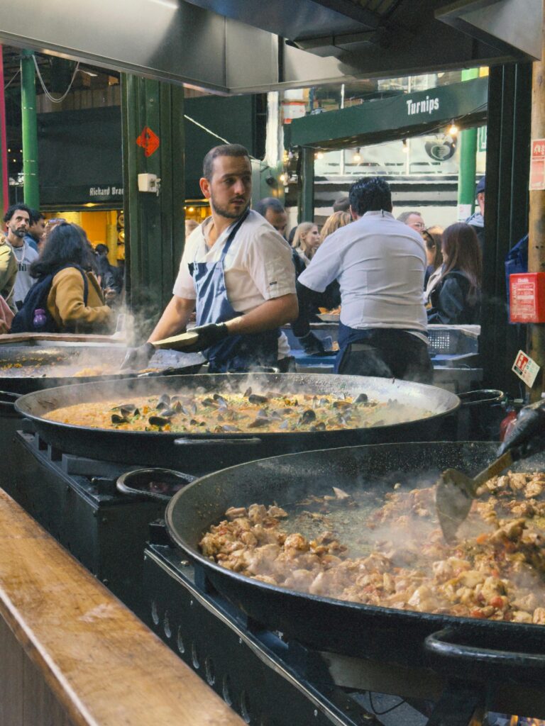 A vibrant street food stall at Borough Market in London with chefs cooking authentic dishes.